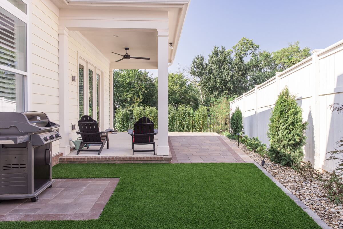 The same side yard finished, with a paver patio, level green surface and an evergreen and river rock border