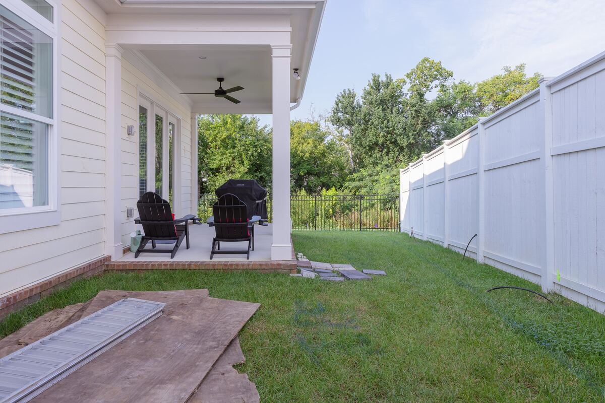 Bare side yard with patchy grass and construction boards beside a covered porch