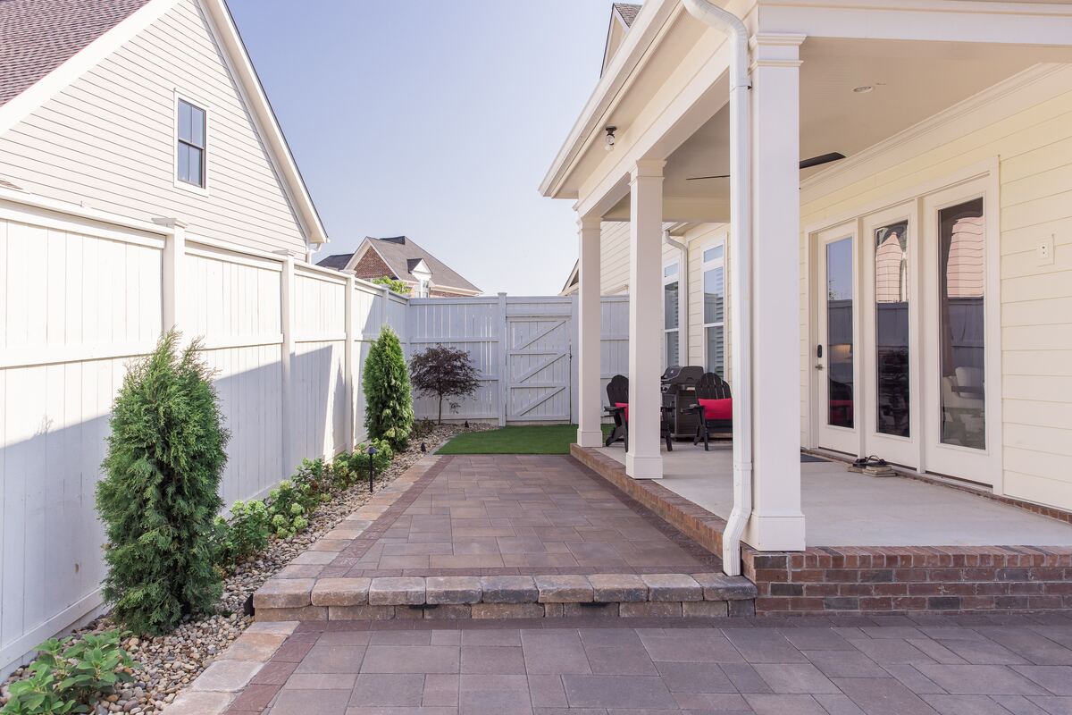 The same strip rebuilt as a paver walkway with evergreen screening and path lighting