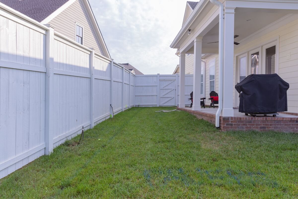 Narrow strip of uneven grass running between a fence and the house