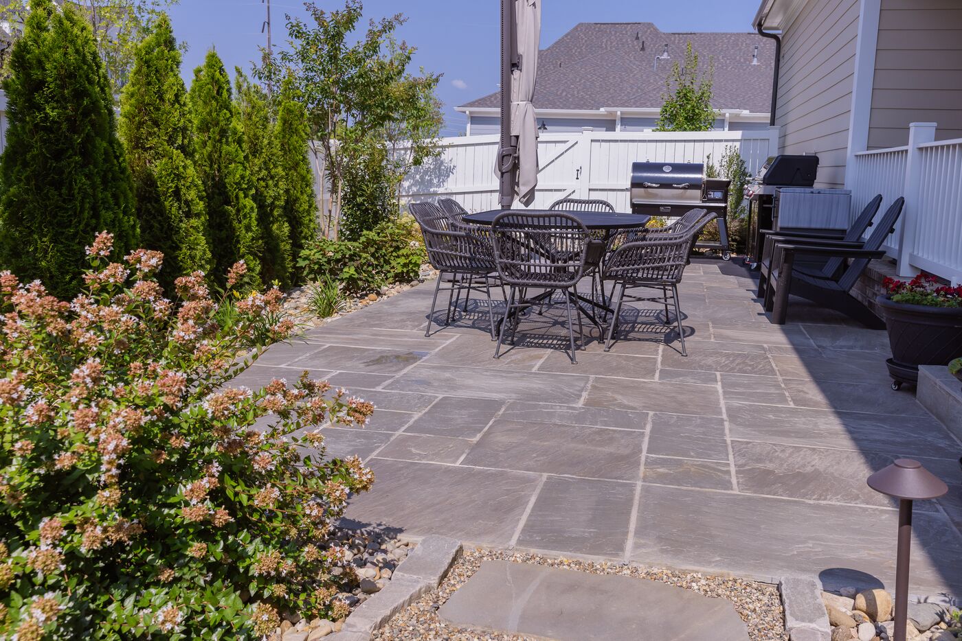 Flagstone patio with an outdoor dining set and evergreen border planting