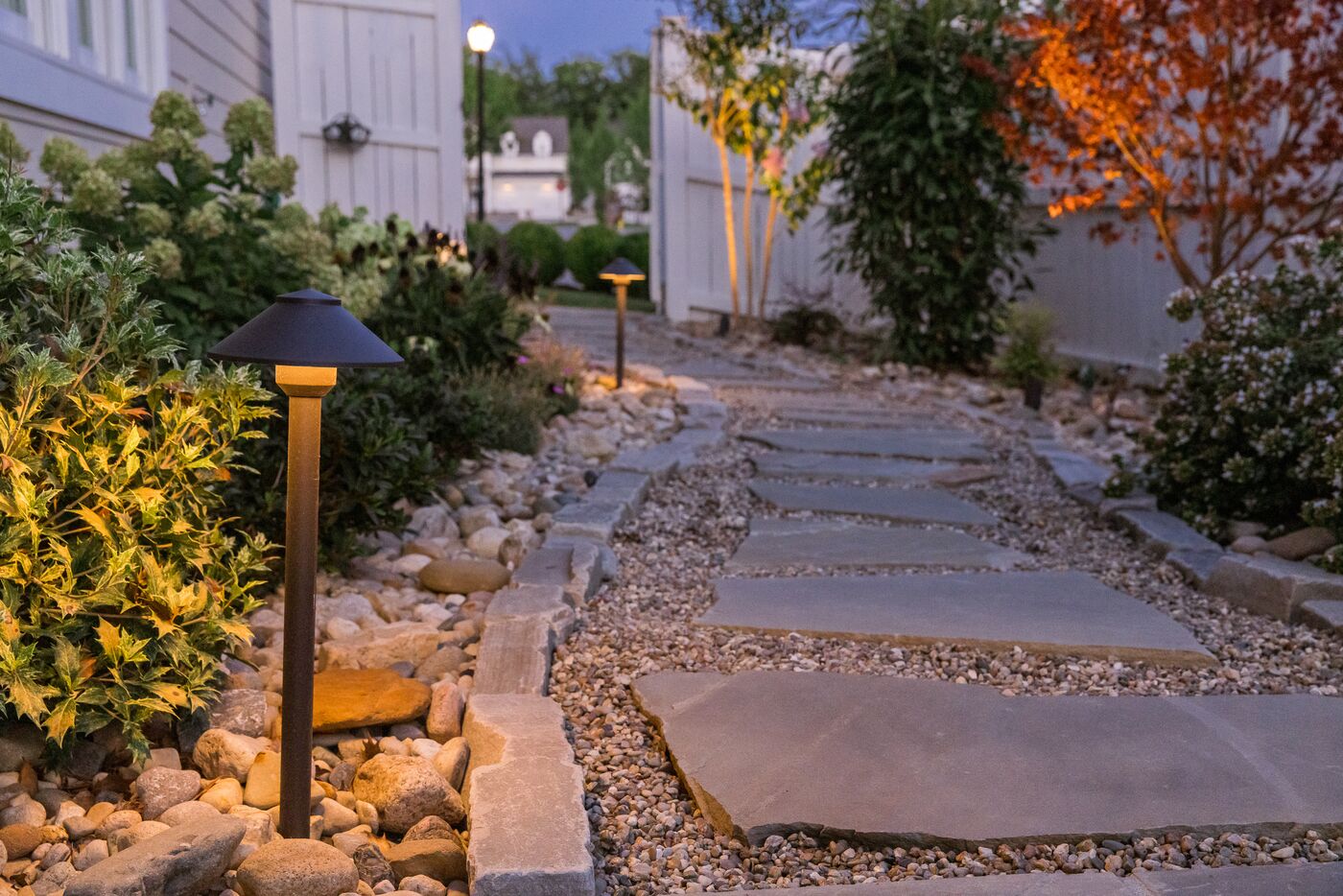 Flagstone path lit by low-voltage path lights at dusk, with uplit shrubs