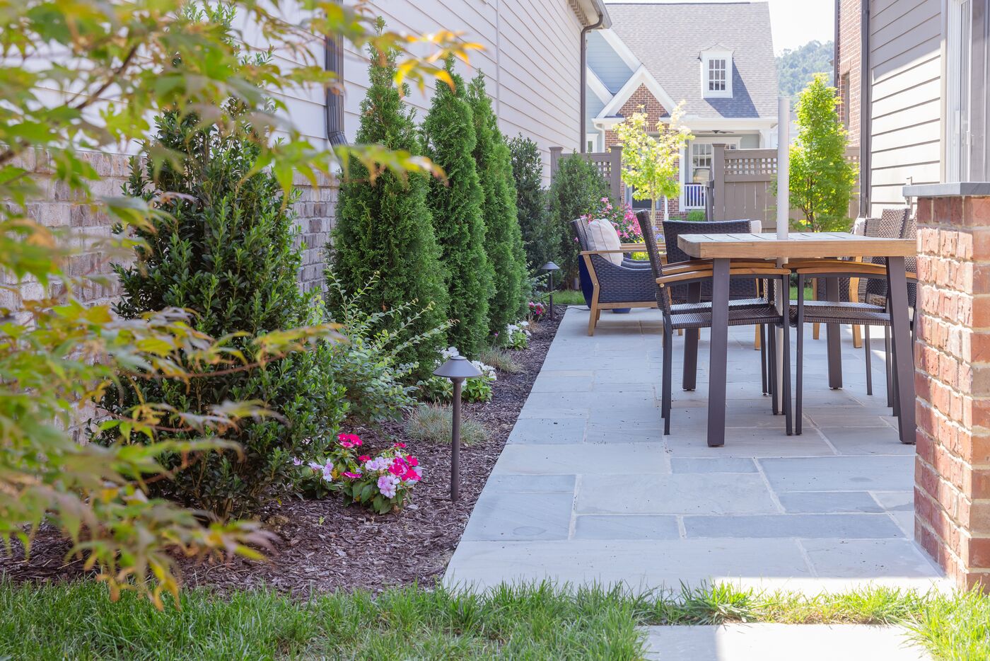 Stone patio with an outdoor dining table, screened by a row of evergreens