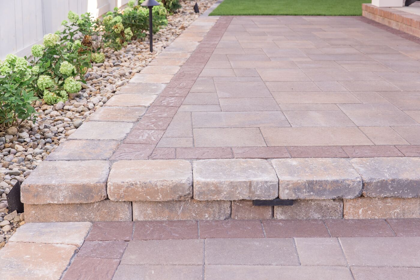 Paver walkway rising to a patio over a cut stone step and riser