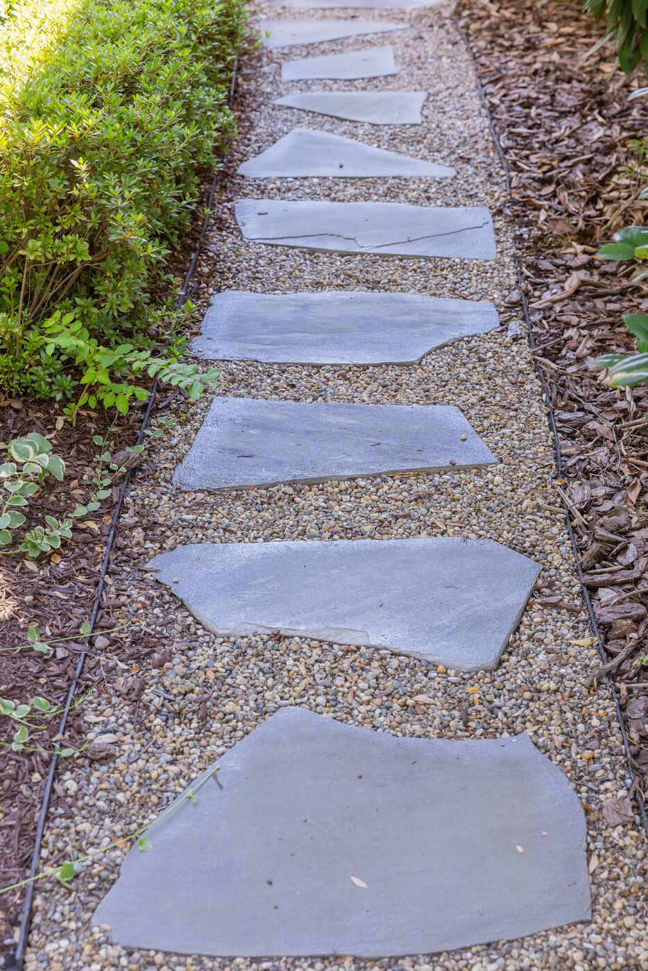 Cut bluestone stepping stones set in pea gravel between planted borders