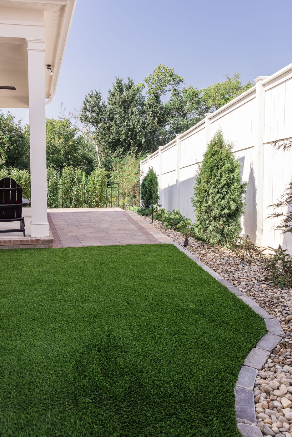 Cobblestone edging separating a lawn from a river rock border along a fence